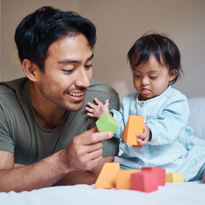 Baby, down syndrome and learning on a bed with child and father playing